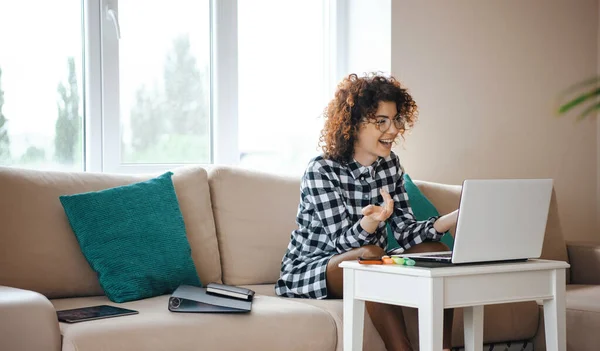 Woman sitting on sofa in front of computer communicating with people in an online conference. Quarantine lifestyle — Stock Photo, Image