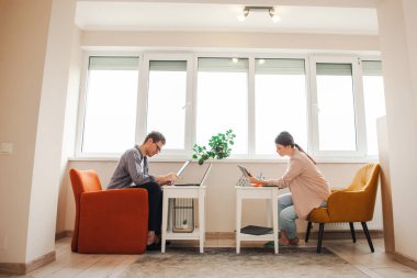 Salgın yüzünden evde çalışan bir çiftin yan görüntüsü. Kanepede birbirimizin önünde duruyoruz. Uzaktan çalış.