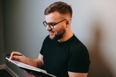 Beyaz duvar arkasında kitap okuyan, gözlük takan, gülümseyen sakallı adamın yan görüntüsü. Meslek.