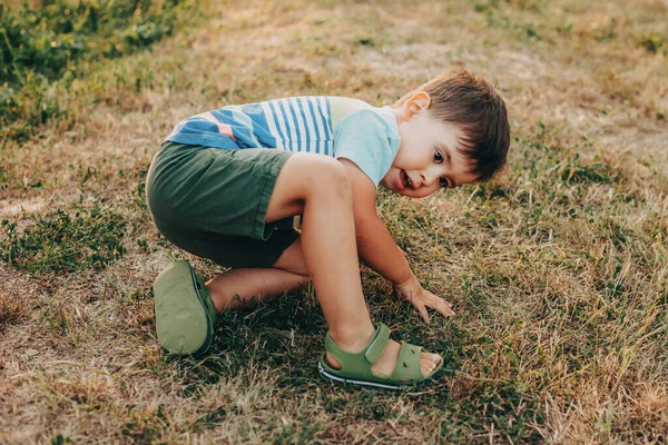 Retrato de um menino caucasiano que caiu no parque e tenta se levantar. Infância cheia de aventuras. Férias passadas fora — Fotografia de Stock
