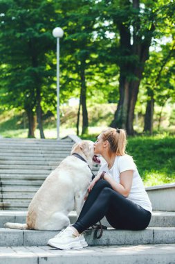 Merdivenlerde köpek labradoruyla oturmuş öpüşen ve sarılan bir kadının portresi. Sabah yürüyüşleri. İnsan ve köpek arasındaki dostluk.