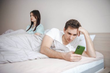Yatakta yatan bir çift, üzgün oturan genç bir eş... Kocasının uyku saatinde akıllı telefon kullanması...