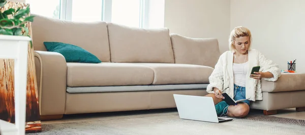 Caucasian woman search learning content online using phone writing up thesis to copybook. Sitting on floor at living room get distant education. Pandemic — Stock Photo, Image