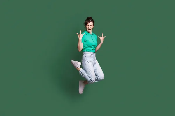 Повнорозмірне фото молодої божевільної жінки, яка стрибає з язиком. Рокенрольний знак. Ізольований на зеленому тлі — стокове фото