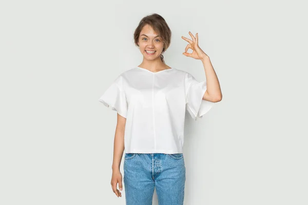 Jovem branca sorrindo menina mostrando OK sinal no fundo branco, olhando para a câmera. gesto da mão. — Fotografia de Stock