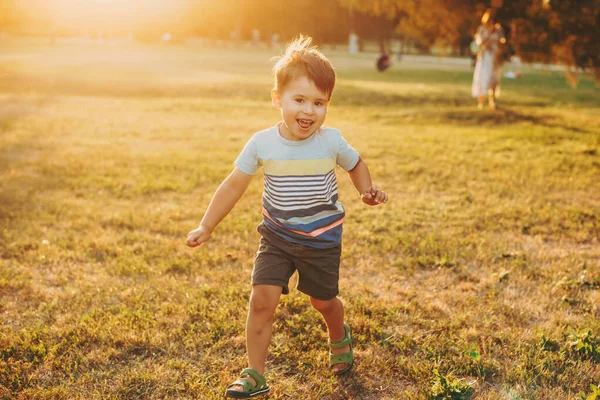 O rapaz caucasiano corre ao longo do campo, filmado. Infância. Vista frontal. Pôr do sol. — Fotografia de Stock