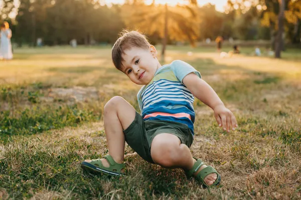 Parkta düştükten sonra kalkmaya çalışan bir çocuğun portresi. Yeşil çim tarlası. Aktif yaşam tarzı sporu. Sağlıklı yaşam tarzı. — Stok fotoğraf