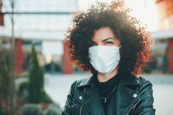 Portrait curly woman in white medical protective face mask looking away while standing on street. Coronavirus prevention. Wearing protective mask. Pretty young — Stock Photo, Image