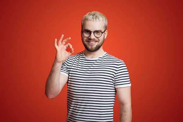 Kaukaski brodaty mężczyzna noszący okulary pokazujące ok znak z dłoni i palców odizolowanych na czerwonym tle uśmiechnięty pozytywny — Zdjęcie stockowe