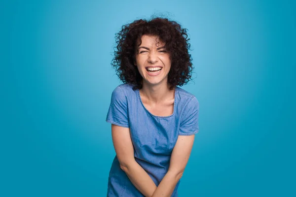 Ritratto di una donna dai capelli ricci che ride posando sullo sfondo blu. — Foto Stock