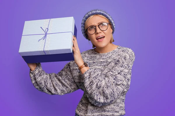 Primer plano retrato de una mujer agitar curiosa caja de regalo mirando hacia arriba aislado sobre fondo de color púrpura. Año nuevo. — Foto de Stock