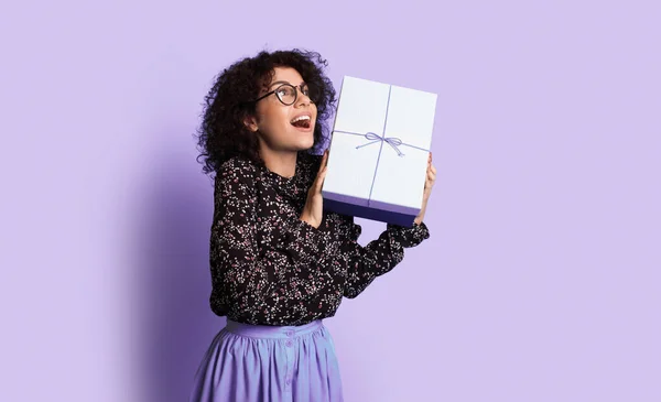 Mujer en un vestido y gafas con caja de regalo en una habitación aislada sobre un fondo púrpura. Vestido casual. Caja de regalo. — Foto de Stock