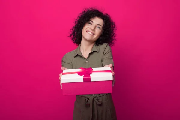 Primer plano retrato de una mujer sosteniendo caja de regalo con lazo de cinta de satén rosa aislado sobre fondo rosa. Mujer caucásica de pelo rizado. Regalo de vacaciones sorpresa — Foto de Stock