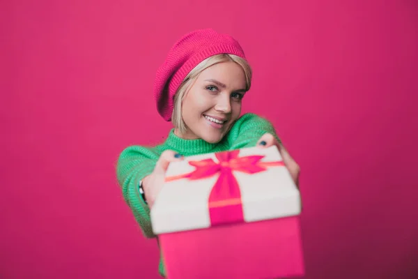 Retrato de cerca de una mujer excitada en una boina rosa sosteniendo la caja extendiendo las manos a la cámara aislada sobre un fondo rosa. Haciéndote un regalo. Navidad. Regalo festivo — Foto de Stock
