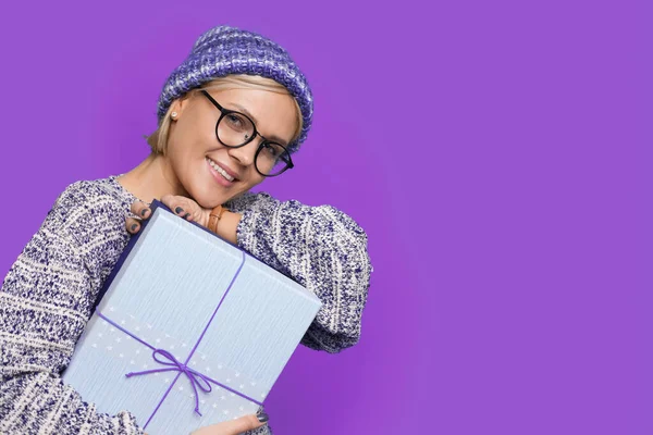 Retrato de cerca de una mujer caucásica emocionada abrazando regalo presente mientras mira a la cámara aislada en el fondo de color púrpura con copyspcae. — Foto de Stock