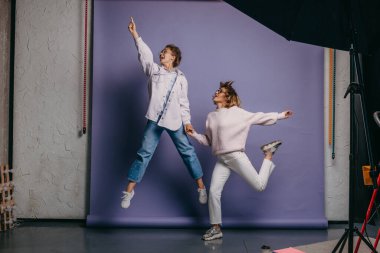 Sıradan giyinen iki kadın, izole edilmiş mor bir arka plana atlıyor. El ele. Arkadaşlık..