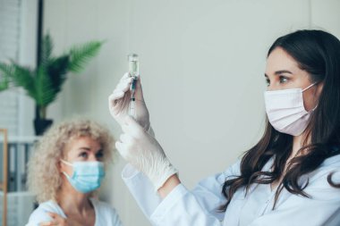 Hemşire elinde şırınga tutuyor ve tıbbi maske takarak Covid-19 aşısı yapıyor. Virüs koruması. Tıbbi üniforma. Doktor eli. Corona virüsü