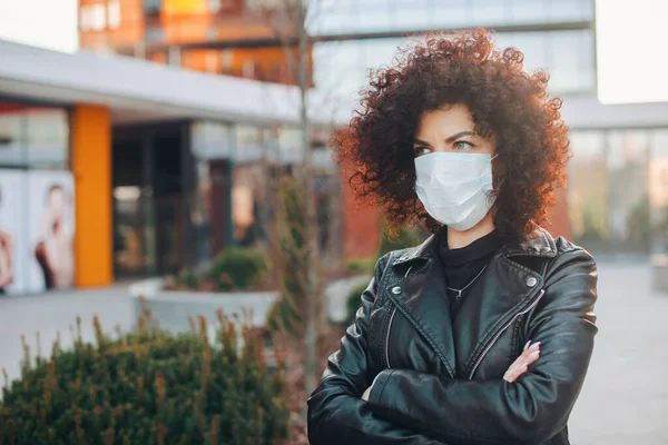 Et nært portrett av en krøllete forretningskvinne som poserer med en medisinsk maske. Kryssede hender. Forretningskvinneportrett. Beskyttelsesmaske – stockfoto