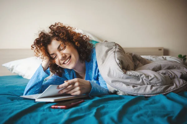 Mujer caucásica leyendo algo durante el tiempo libre en el dormitorio. Cara sonriente. Coronavirus — Foto de Stock