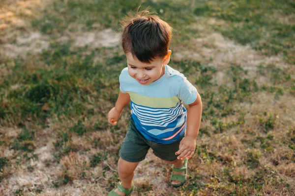 Gülümserken çimlerin üzerinde koşan beyaz bir çocuğun en iyi görüntüsü. Yeşil çim tarlası. Hafta Sonu — Stok fotoğraf