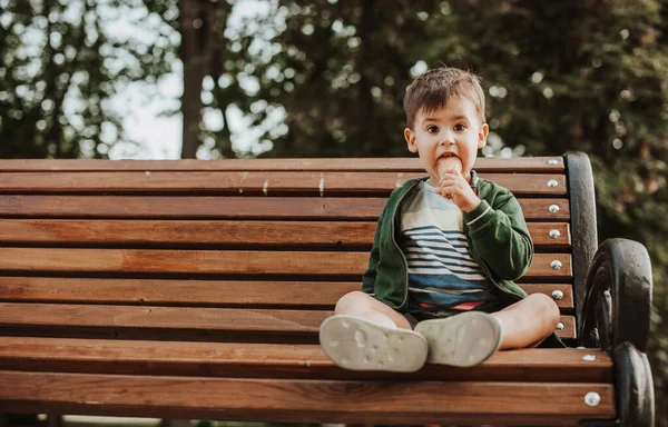 Beyaz çocuk bütün gününü parkta dondurma yiyerek ve bankta oturup kameraya bakarak geçiriyor. Boşluğu kopyala — Stok fotoğraf