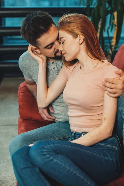 Retrato de um homem caucasiano beijando mulher ouvida vermelho enquanto sentado em poltrona. Uma fêmea carinhosa. Relacionamentos. — Fotografia de Stock