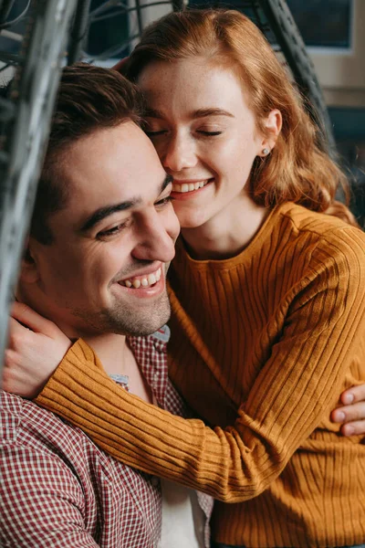 Retrato de cerca de una pareja sentada en un sofá abrazándose y sonriendo. Sala de estar interior. Cara feliz. Amor. —  Fotos de Stock