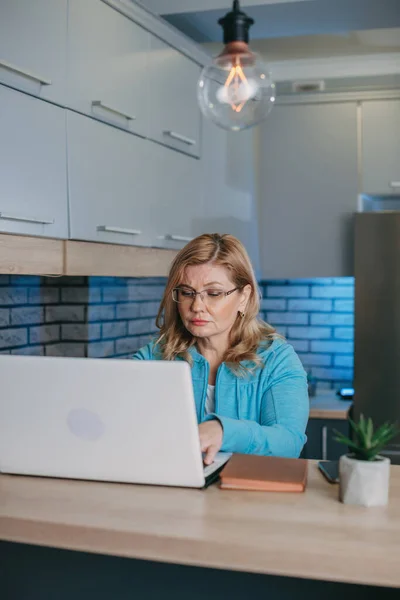 Shot of a focused middle-aged businesswoman in glasses sitting in front of laptop and working. Quarantine lifestyle. Blonde haired woman. — Stock Photo, Image