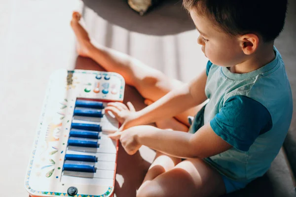 Vista superior de um menino sentado no chão e tocando com um piano de música de brinquedo de plástico. Brinquedo colorido. — Fotografia de Stock