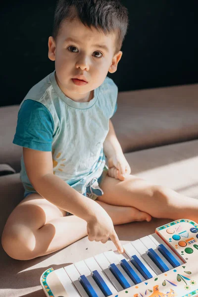 Vista frontal de um menino tocando um piano de brinquedo enquanto aprende música, sentado no chão. — Fotografia de Stock