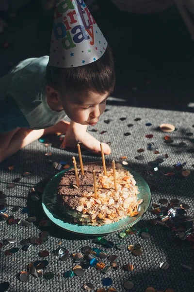 Petit garçon célébrant son anniversaire et soufflant des bougies sur le gâteau, à l'intérieur. Vacances, anniversaire. Aliments sucrés. — Photo