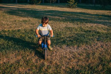 Tarlada bisiklet süren beyaz bir çocuğun ön görüntüsü. Sağlıklı bir yaşam tarzı. Açık hava yaz eğlencesi. Açık hava eğlencesi. Spor oyunu. Yeşil çimen alanı.