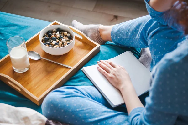 Mujer escribe en gran cuaderno blanco abierto, sentado en la cama en pijama azul con desayuno con avena. Vista superior. Rutina. Estilo de vida saludable. Buenos días. — Foto de Stock