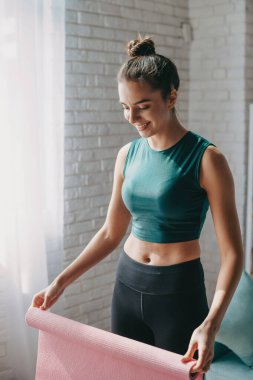 Yoga yapmadan önce beyaz kadın, egzersize hazırlanma, yoga minderi açma, spor giysi giyme. Sağlık hizmetleri. Vücut bakımı.