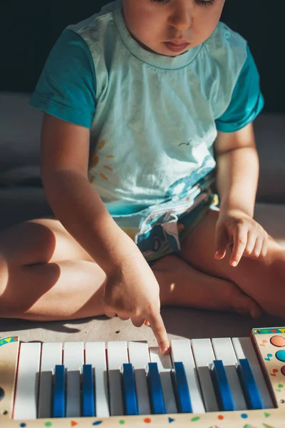 Front view of a caucasian boy sitting on the floor and playing with a plastic toy music piano — Fotografia de Stock