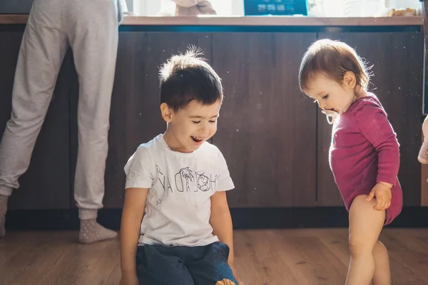 Due bambini figlia e figlio si divertono a giocare a giocattoli sul pavimento della cucina. I bambini giocano. Babygirl. — Foto Stock