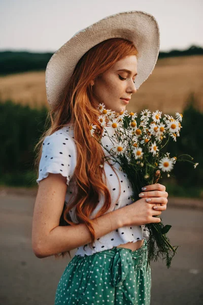 Redhead woman with a large bouquet of wildflowers walking along rural road — Zdjęcie stockowe