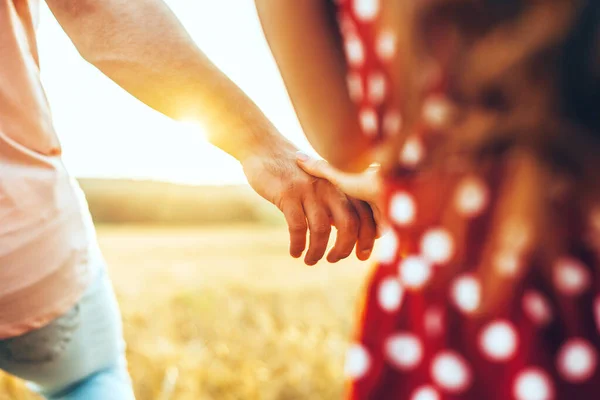 Närbild porträtt av ett par som håller händer medan du går genom ett vetefält vid solnedgången. Naturlandskap. Vetefält. Majsfält. Sommarsemester. — Stockfoto