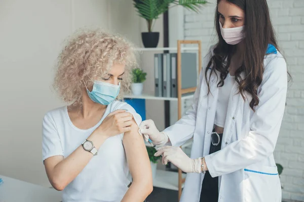 Dokter kaukasia bertopeng medis dan sarung tangan memberikan vaksin untuk bahu pasien. Wanita mendapatkan vaksinasi. Imunisasi virus Corona. Coronavirus — Stok Foto