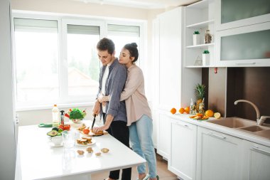 Gülümseyen kız arkadaş adama arkadan sarılıyor ve onu sağlıklı yemeği hazırlarken izliyor. Sağlıklı yemek, diyet.