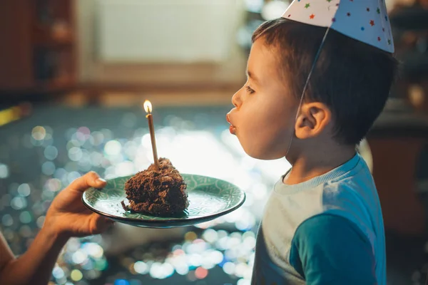 Sidovy över en fyraårig grabb som blåser ljus på skiva hembakad tårta. Firar födelsedag. Födelsedagsfest för barn. — Stockfoto