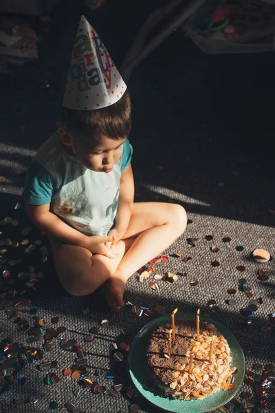 Top view of a caucasian boy sitting on floor and blowing birthday candles out. Holiday, birthday. Sweet food. Birthday party. — Fotografia de Stock