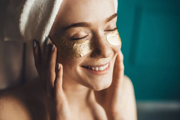 Close-up portret van een vrouw met een handdoek op het hoofd die haar huid verzorgt met onder-ooglapjes. Verjongingsbehandeling. Gezichtsbehandeling. Gezondheidszorg. — Stockfoto