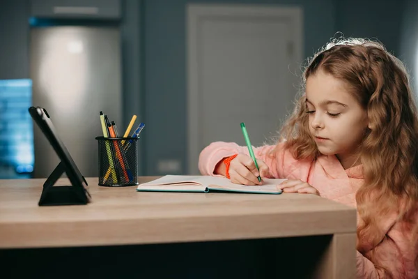 Chica caucásica haciendo la tarea sentada en el escritorio en su habitación escuchando una lección de audio en la tableta. E-learning, concepto de educación en el hogar. Tecnología de Internet. Clase de escuela. —  Fotos de Stock