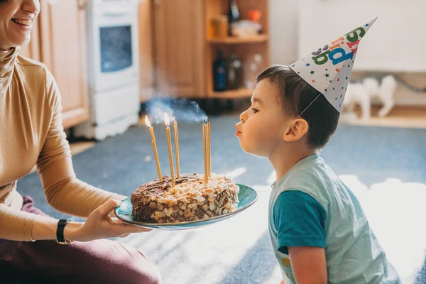 Widok na białego chłopca zdmuchującego świeczki na torcie urodzinowym na imprezie. Świece płoną. Święta, urodziny. Słodkie jedzenie. — Zdjęcie stockowe