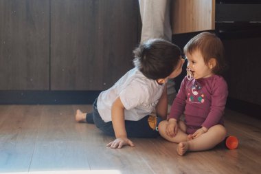 Erkek ve kız kardeş yerde oynuyor. Erkek kardeşler kız kardeşlerini sever.