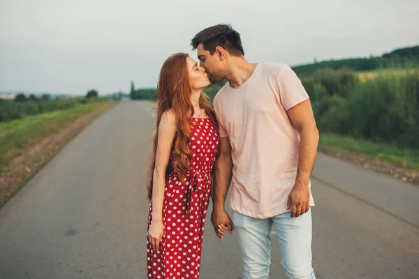 Portrait of a couple kissing in the middle of a rural road on the background of natural landscape. Summer road trip. Countryside landscape. Family day. — Foto Stock