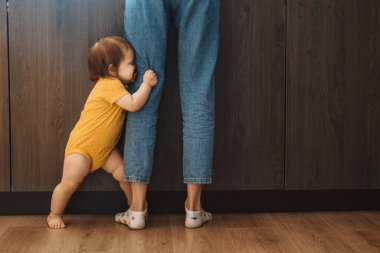 Bebek kız mutfakta annesinin bacaklarının arkasına saklanıyor.