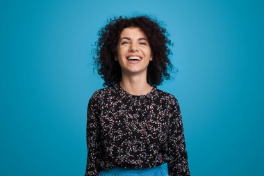 Mavi arka planda izole bir şekilde gülümseyen kıvırcık saçlı beyaz bir kadının portresi. Yakından bir portre. Pozitif kişi. Güzel manken..