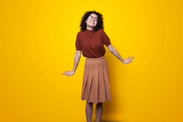 Mulher caucasiana de cabelos encaracolados usando óculos posando com expressão facial feliz isolada sobre fundo amarelo. — Fotografia de Stock